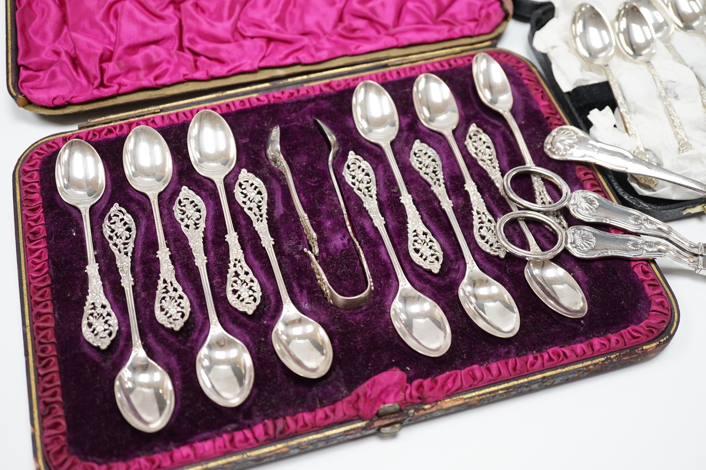 A cased set of twelve Victorian silver teaspoons, with pierced terminals by William Comyns, London 1889, with a damaged pair of matching sugar tongs, a cased set of six later teaspoons, a pair of George IV silver King's
